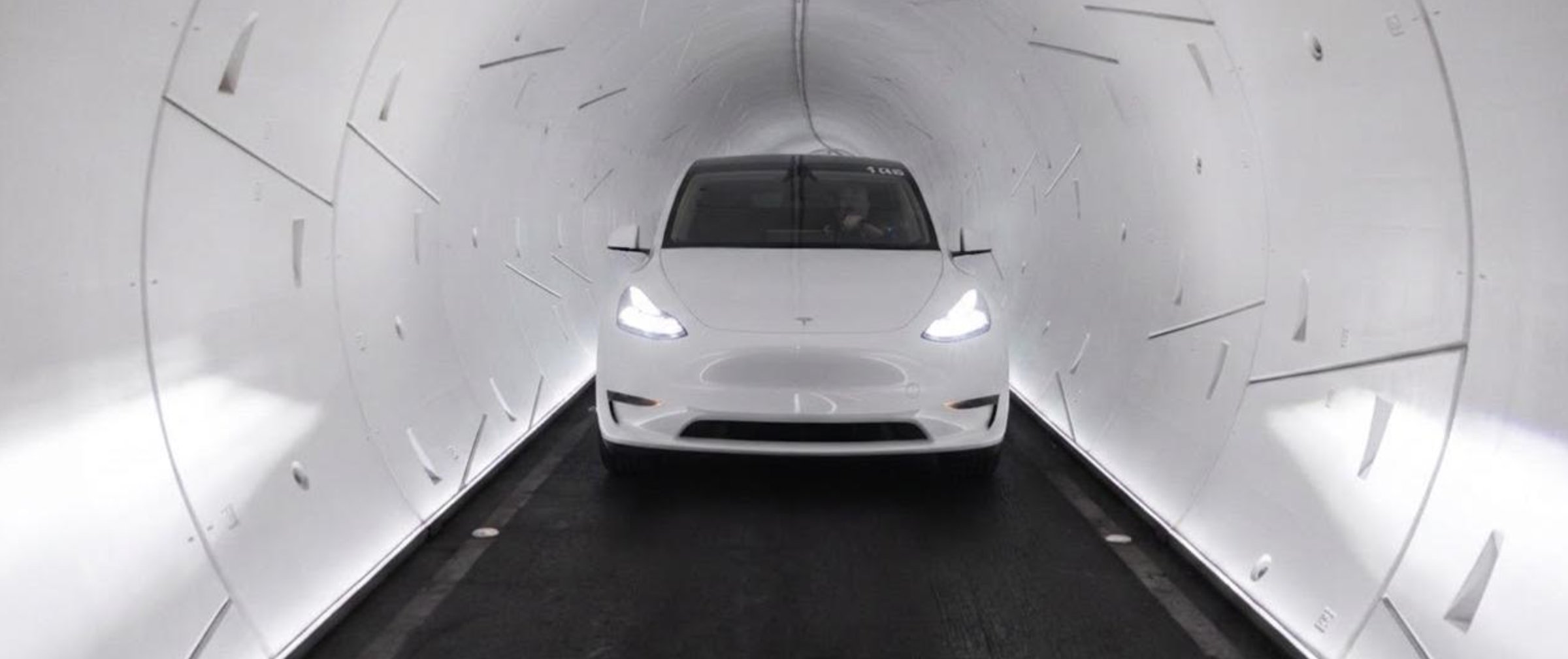 A white Tesla Model Y with headlights on in a brightly lit white Loop tunnel